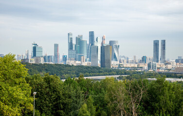 Fototapeta premium Modern Skyline of Moscow City Commercial District with Skyscrapers and Verdant Trees Under Overcast Sky, Moscow, Russia, 9 August 2025