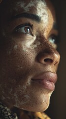 Freckles vitiligo adult cisgender woman with dark skin and white cream on her face looks thoughtful in a close up studio portrait with soft lighting