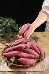 Fresh Purple Sweet Potatoes in Rustic Kitchen Setting with Woman's Hand and Wicker Basket