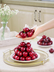 Fresh Red Cherries on Serving Tray with Hand Holding Fruit in Bright Kitchen Interior