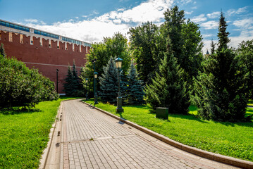 Serene Park Path Near Kremlin Red Brick Wall With Lush Trees, and Vintage Lampposts Under Sunny Sky, Moscow, Russia, 9 August 2025