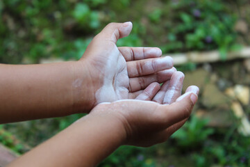 close up of child's hand with open palm covered in white powder, outdoors with blurred green background