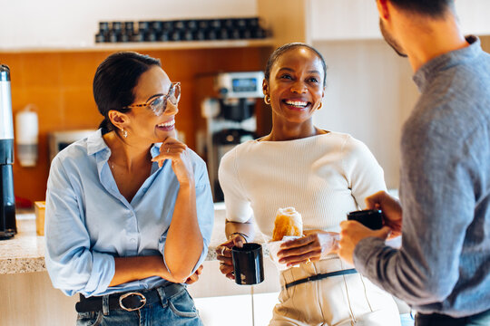 Group of coworkers chatting informally while enjoying coffee in the office kitchen