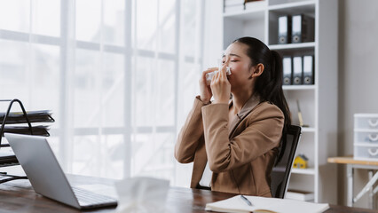 Young asian businesswoman sneezing at office desk