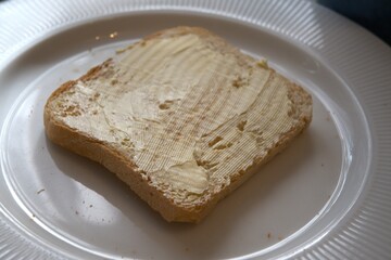 Close-up view of toasted bread slice spread with margarine on white plate.