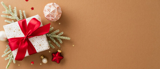 Christmas gift box with red ribbon surrounded by festive ornaments and pine branches on brown...