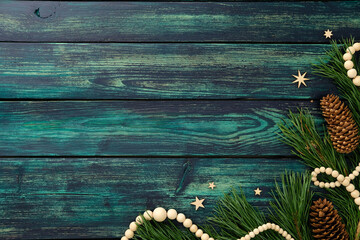 Rustic Christmas flat lay with pine branches, pinecones, wooden beads, and stars on teal wood...