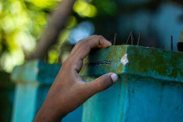 A hand touching a weathered turquoise wall with green moss