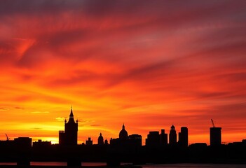 Naklejka premium Iconic London skyline silhouette at sunset, dark against fiery sky, design, cityscape