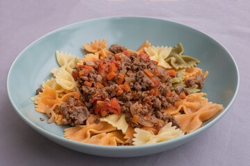 Italian cuisine close-up. Farfalle pasta with ground beef, tomato, onion and carrot ragù. Homemade cooked dish, authentic recipe, delicious comfort food background for culinary themes.