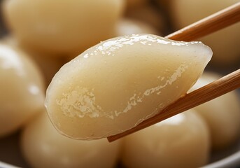 Pickled garlic cloves held by chopsticks against blurred background