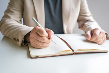 Businessman wearing jacket writing on notepad. Close up view.