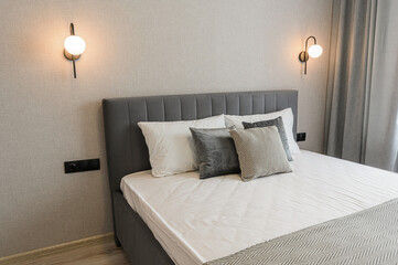 A modern bedroom features a gray upholstered bed with white linens and decorative pillows, flanked by globe sconces against a textured wall