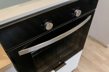 A close-up shows a modern black oven with a stainless steel handle and control knobs. It's built into white cabinets