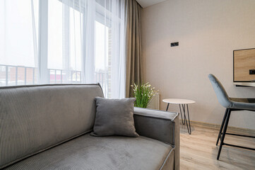 A cozy living room is shown, featuring a corduroy sofa with a matching pillow, a small round table, and a sleek gray chair. Neutral tones and natural light create a serene atmosphere