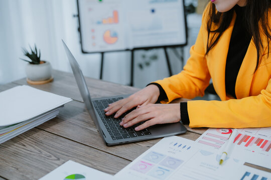 Young happy asian businesswoman in suit using tablet for video conference and holding smartphone, working with financial graphs and charts, sitting at desk in modern office