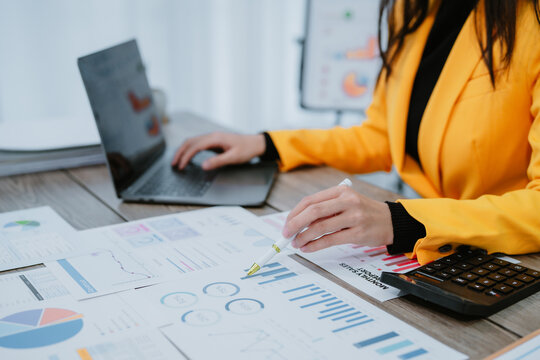 Young happy asian businesswoman in suit using tablet for video conference and holding smartphone, working with financial graphs and charts, sitting at desk in modern office