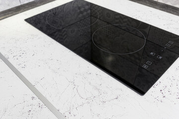 A sleek, black induction hob sits flush against a light, marble-patterned countertop in a modern...