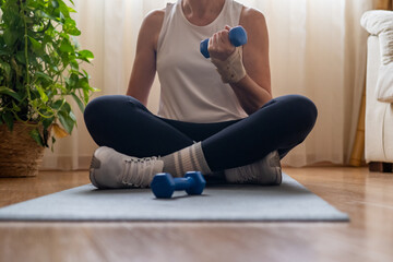 Mature woman lifting hand weights in living room, wearing wrist brace for safe home training and injury prevention during daily workout session
