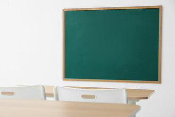Blank green chalkboard, desks and chairs in classroom