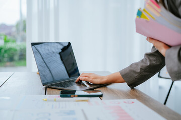 Asian businesswoman working with documents in office taking notes on clipboard surrounded by paperwork