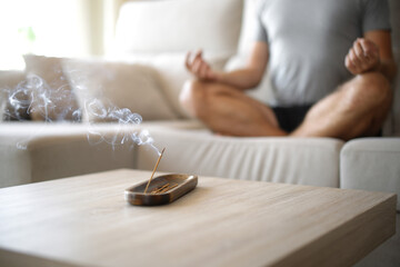 Man doing yoga with incense stick burning in foreground at home