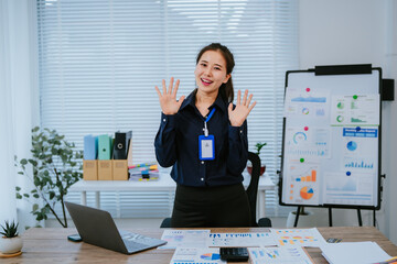 Young Asian businesswoman holding a pen and clipboard, analyzing statistical data on a tablet screen while working on a computer in a modern office environment