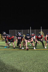 Naklejka premium Football players in black and red uniforms ready to start the game on a floodlit artificial turf field at night