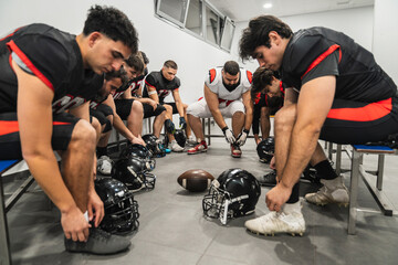 Team of american football players getting ready in the locker room, lacing up cleats before a game. Focus on preparation and teamwork