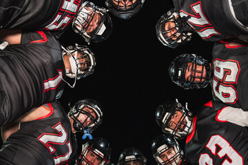 American football players wearing jerseys and helmets, standing in a huddle, strategizing on a dark background