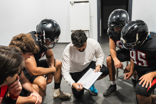 American football coach showing strategy on a clipboard to his team in a locker room, focusing on teamwork and planning