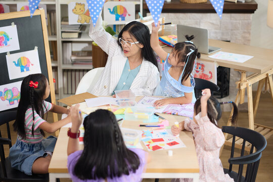 A teacher with students in the classroom during drawing and painting lesson. The teacher is wearing glasses and guiding them to draw in a creative way - Powered by Adobe