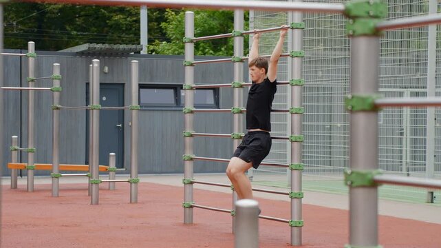 Hanging Leg Raise - Man Hangs From The Bars, Lifting His Knees To His Chest At The Outdoor Gym. - wide shot