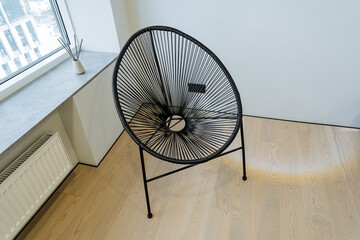 Inside a cozy room, a sleek black chair is elegantly positioned on a polished wooden floor, conveniently located next to a large window that allows an abundance of natural light to flood in