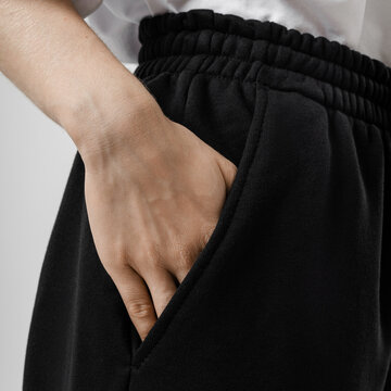 Close-up of a woman&rsquo;s hand in pocket of black sweatpants against neutral studio backdrop, showing texture and detail.
