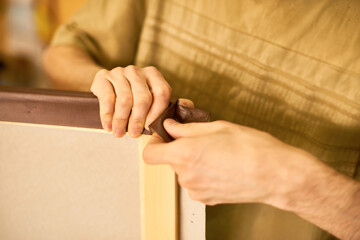 Man stretching canvas over wooden frame, hands gripping fabric tightly while assembling artwork, focus on precise manual technique, partial body visible