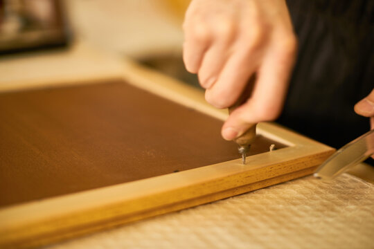 Man using screwdriver to fasten screw into wooden frame, close up of hands working on carpentry project, demonstrating manual craftsmanship and precision