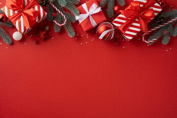 Vibrant red background with evergreen branches and festive gifts wrapped in ribbons creates a warm...