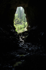Silhouette of a big cave entrance from inside, water stream flowing into cave