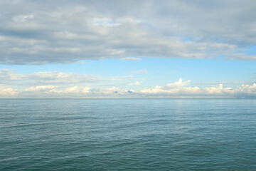 Calm ocean reflecting cloudy sky with gentle waves and ripples on water. Sun illuminates clouds in bright blue sky above sea. Beautiful calm magic seascape. Idyllic, picturesque wild nature place.