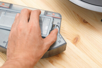 Human takes out a dust container in a robotic vacuum cleaner.