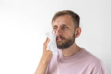 Man with beard wiping face with tissue while looking away, wearing pink t-shirt, concept of fatigue, hygiene and personal care