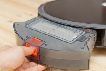 Human takes out a dust container in a robotic vacuum cleaner.