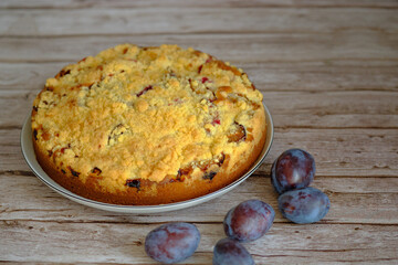 Appetizing homemade plum cake with crumbs on a wooden table. A few fresh plums lie nearby.