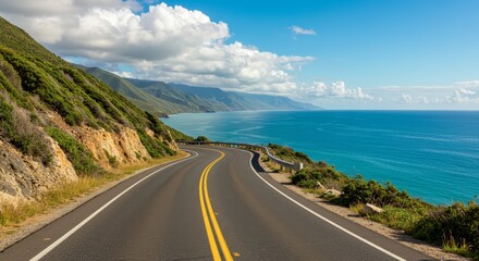 Scenic coastal road view with ocean and mountains under a bright blue sky and clouds