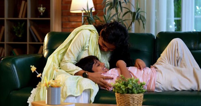 Indian mother tickling son while sitting in modern home on sofa, bonding in quality time together, sharing laughter, affection, love, joy, warmth, parent child relationship, family lifestyle indoors