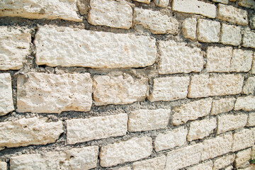Textured wall of rectangular stone blocks in light beige shades and cement between them.
