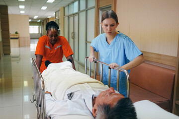 Medical staff team pushing stretcher gurney bed with injured patient to emergency room in hospital. Group of multiracial doctor and nurse work together at professional medical clinic. Health care ward