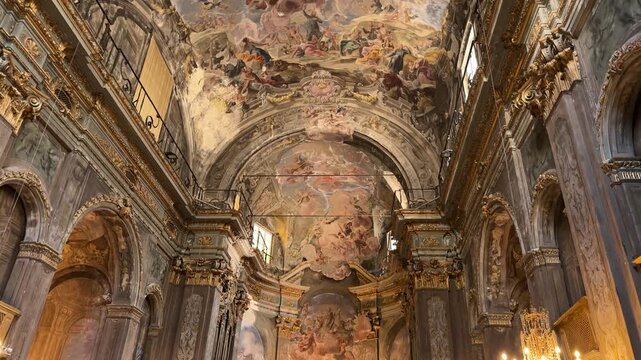 Tilt up shot exploring the ornate Baroque interior and frescoed ceiling of a historic Catholic church softly lit by warm candles in Savona, Italy.