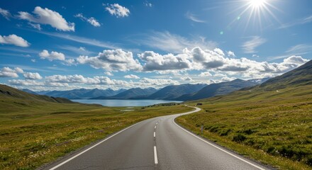 Scenic road winding through green fields under a sunny sky with mountains and a lake in the distance